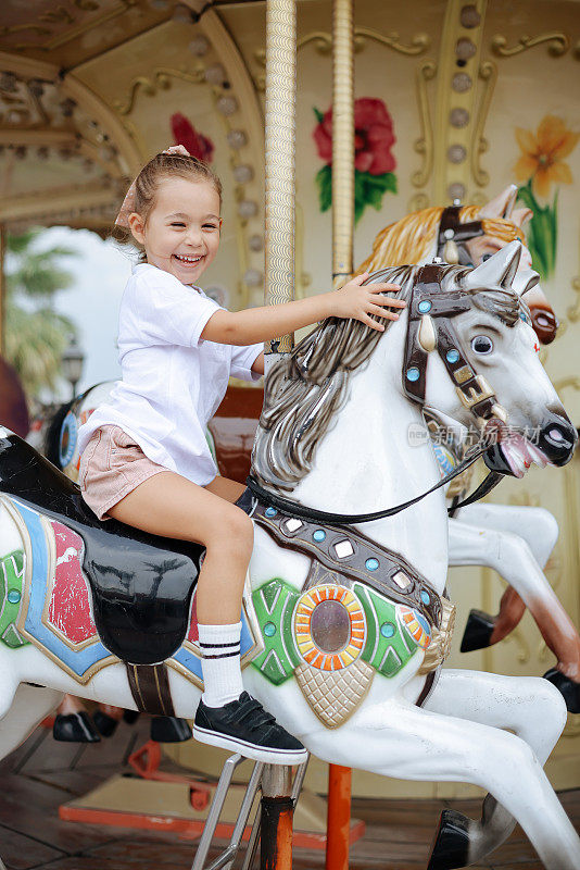 漂亮的孩子骑在旋转木马上。可爱的女孩是骑马的吸引力。有趣的庆祝活动