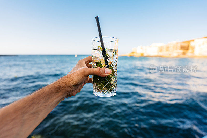 拿着莫吉托鸡尾酒的男子对着蓝海