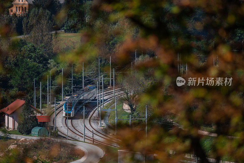 夏日里，现代化的客运动车组列车载着火车车厢，正从林斯克警察火车站飞驰而过。从远处透过树叶看火车。