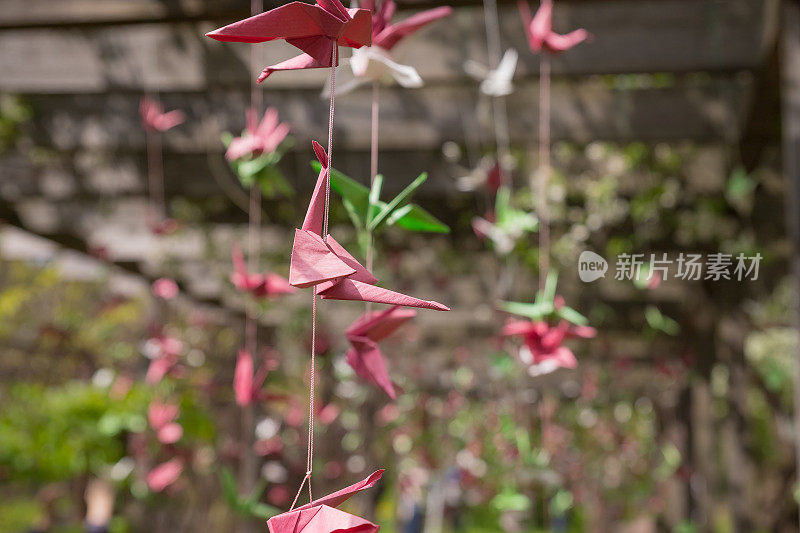 折纸鹤鸟挂在线在花园对着太阳。树上五颜六色的纸鹤。婚礼装饰。日本园林中的纸鸟装饰