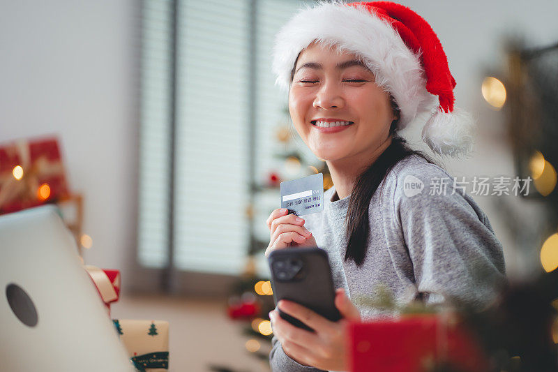 一名亚洲女子开心地微笑着用智能手机和信用卡购买圣诞礼物。