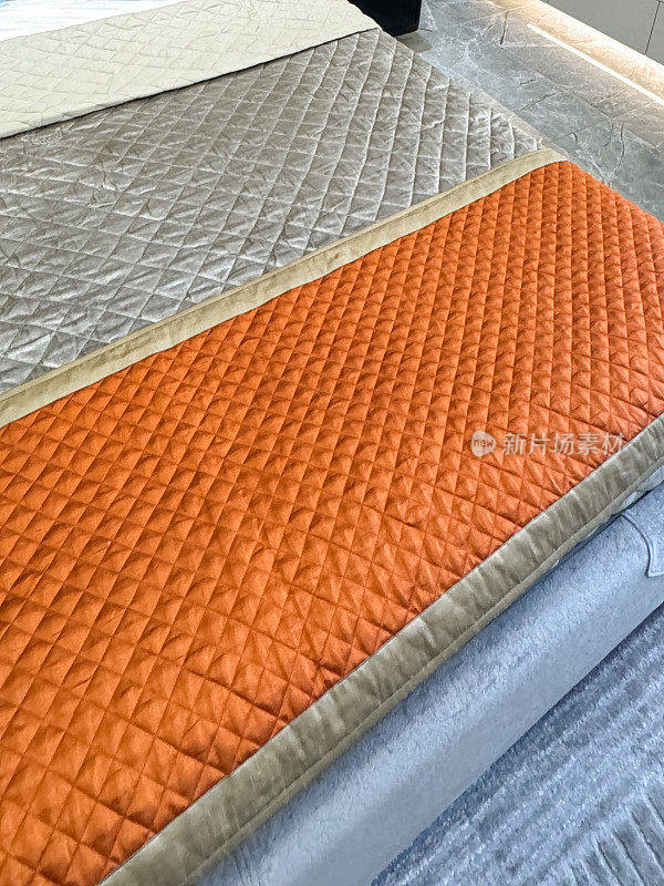 双人床的全画幅图像与绗缝，灰色和橙色的床扔毯，折叠被子盖，重点在前景，抬高的看法