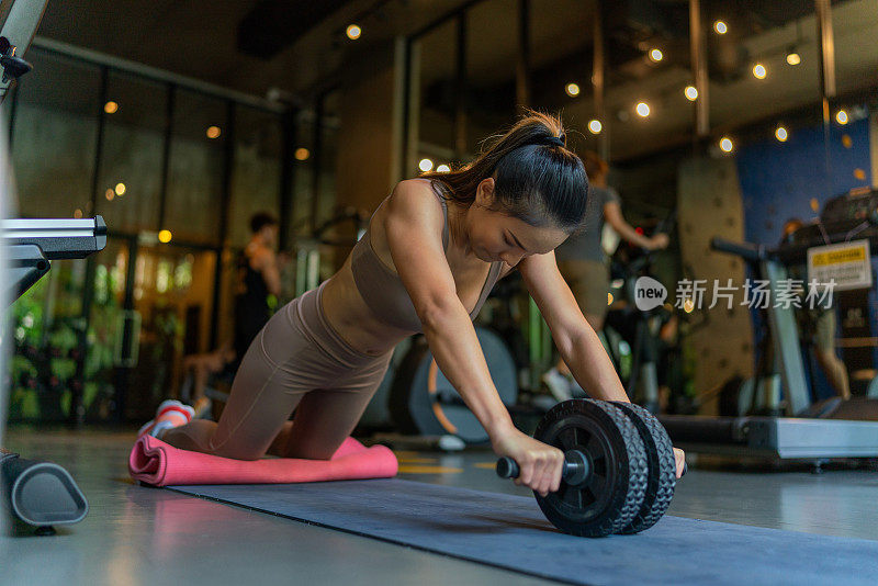 亚洲女性在光线充足的室内健身俱乐部做腹肌轮伸展运动