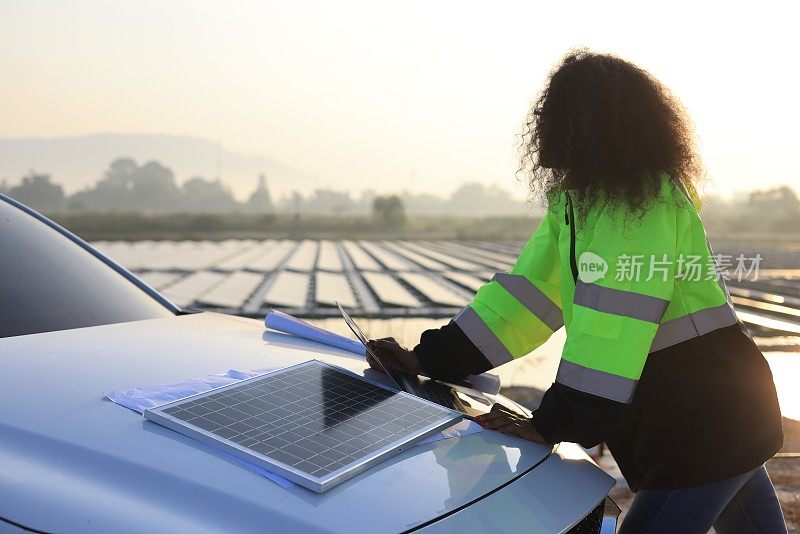 穿着绿色安全夹克的黑人女工程师在漂浮太阳能农场的汽车前引擎盖上工作