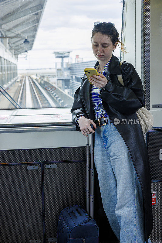 年轻的女商人在肯尼迪机场航站楼处理行李时使用她的智能手机