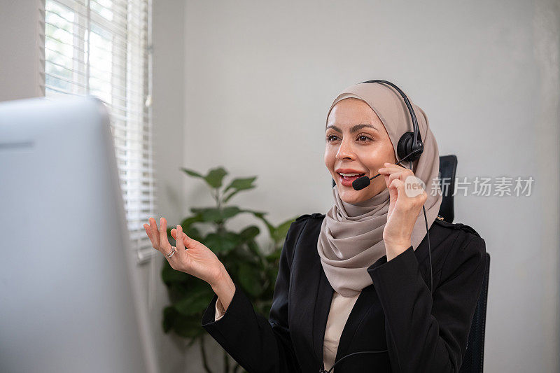 在客服中心，戴着头巾的穆斯林女客服人员正在用笔记本电脑与客户交谈