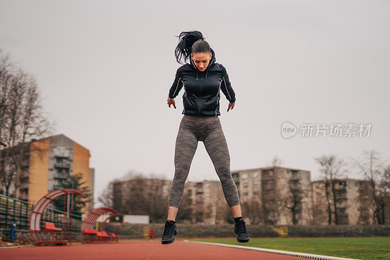 一位年轻的健身女士正在跑道上热身。她跳。