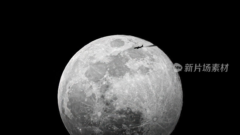 月亮在深黑的天空中升起，一架飞机带着一缕凝结的光飞过