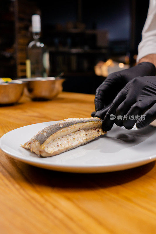 戴着黑色手套的厨师将鱼放在白色盘子上的特写镜头