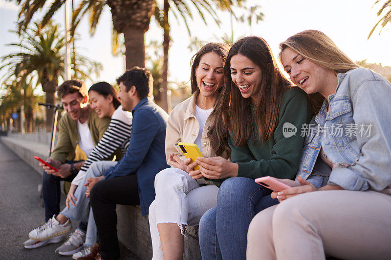 一大群形形色色的z世代朋友微笑着坐在户外使用和看手机。