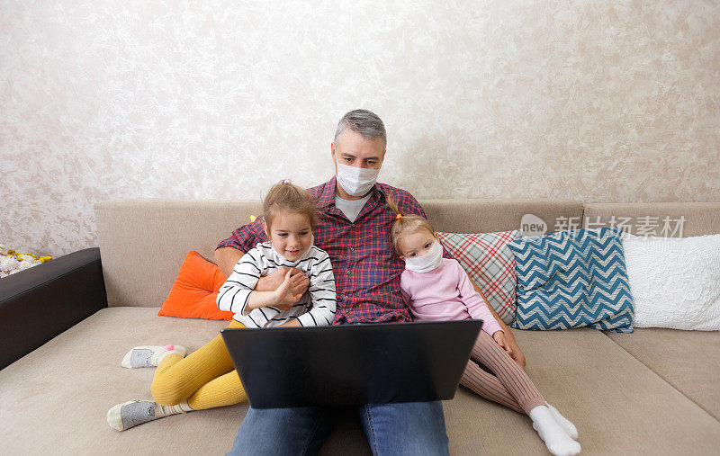 一位年轻的父亲和他的孩子们在家里用一台自我隔离的笔记本电脑工作。全职的概念。Freelance.Telecommuting。