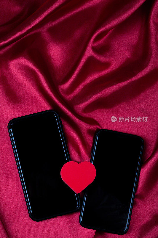 红心和两部手机在红绸布上随波浪起伏。网络约会，拷贝空间，情人节概念。