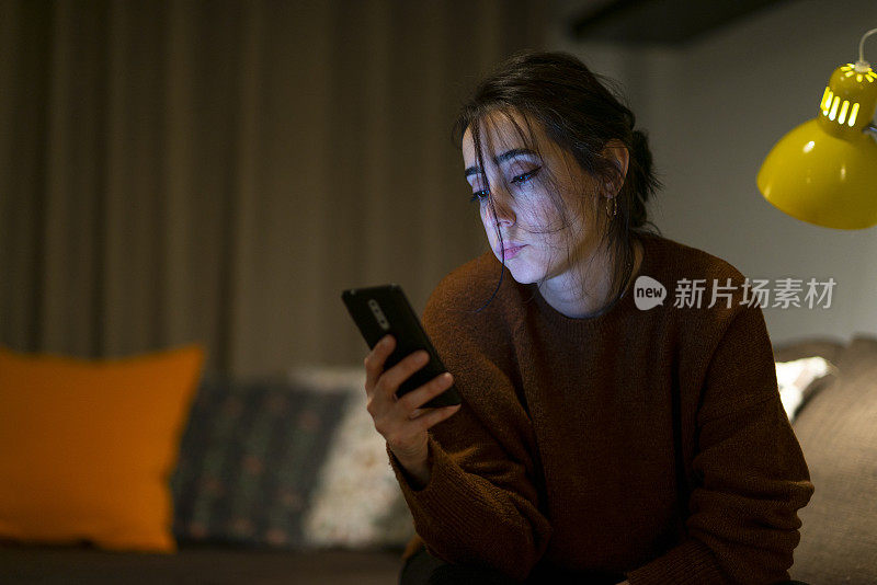 晚上在家看手机屏幕的女人感到心烦意乱。