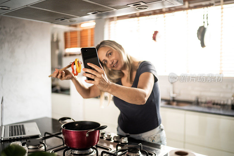 成熟的女人做饭和展示食物在视频通话在家里的智能手机