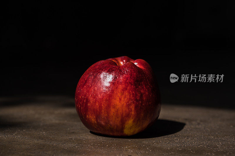 一个红苹果在暗光结构背景下，以一种艺术的方式在自然光下。
