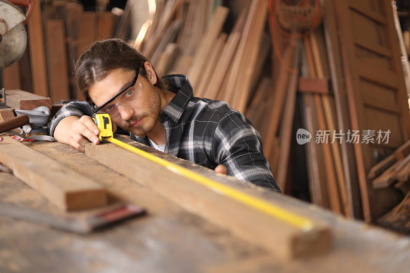 年轻的白人木匠是测量木板在他自己的车库风格的车间的爱好