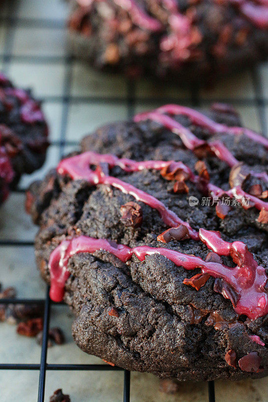 一排排新鲜烘焙的，自制的，巧克力片黑森林饼干，装饰着粉红色的水糖霜，冷却在铁丝上，金属架上面的防油纸羊皮纸，聚焦前景