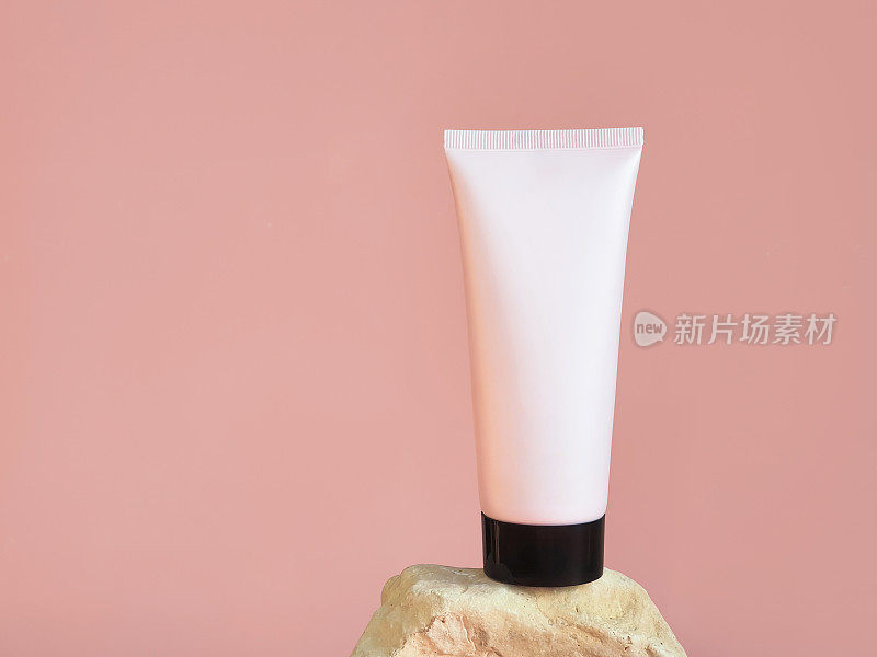 无品牌的粉红色挤压化妆品塑料管与黑色帽在岩石孤立的粉红色背景。瓶的品牌和标签-保湿霜，凝胶，皮肤护理，牙膏，乳液，香脂。模型