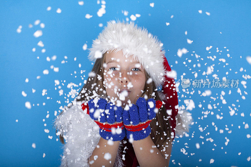 美丽的小女孩戴着圣诞老人的帽子吹着雪花