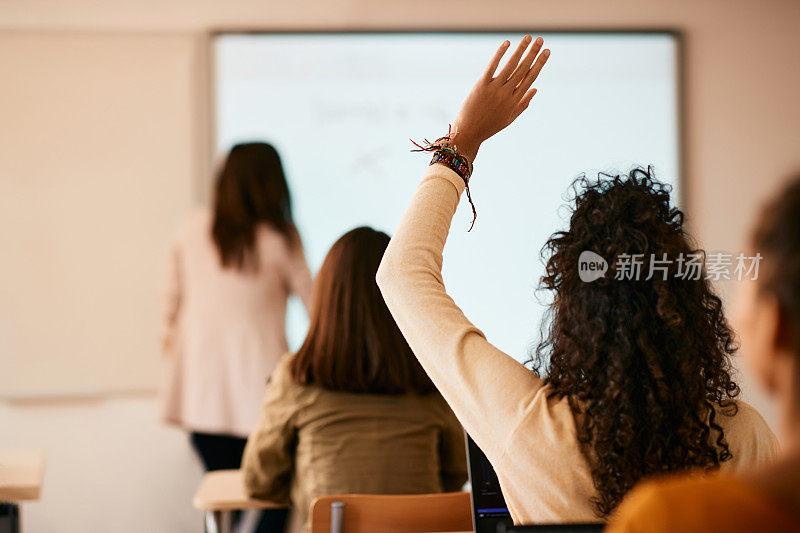 高中学生在教室举起手臂提问的后视图。