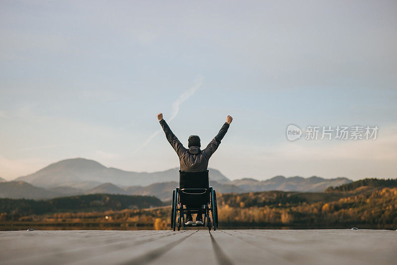 残疾人坐在轮椅上，双手举起，在码头享受大自然