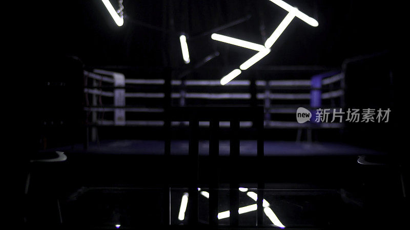 拳击台和两把桌椅的黑色背景。由聚光灯照亮的蓝色绳索包围的常规拳击场的视图。拳台周围的灯光秀。