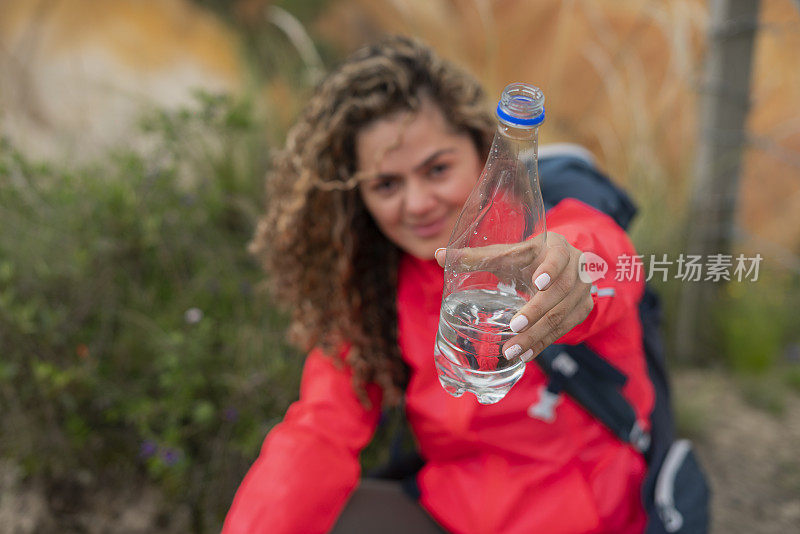 这位拉丁女子坐在被大自然包围的沙漠中央，用水瓶给自己补水