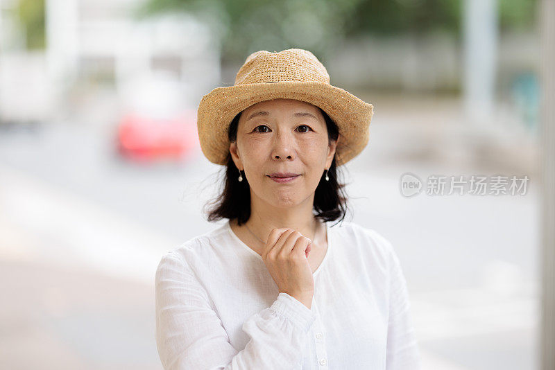 一个微笑的亚洲妇女的帽子看着相机在户外的肖像