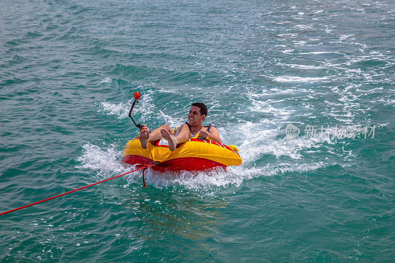 一名男子坐在一艘船拖着的充气环里，手里拿着一台GoPro相机。