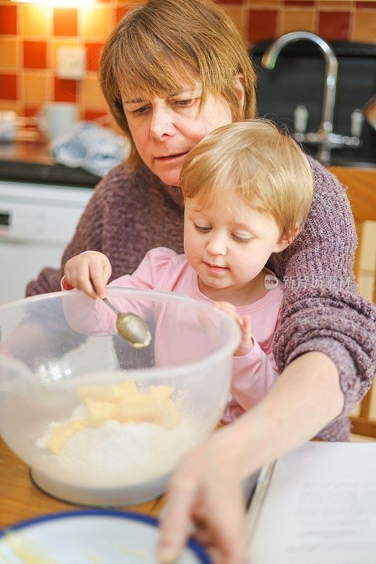 奶奶在厨房的桌子上教她的孙子如何准备蛋糕混合物