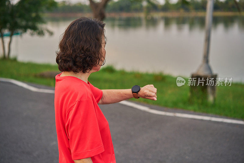 老年妇女在公园慢跑后用智能手表检查心率和方向