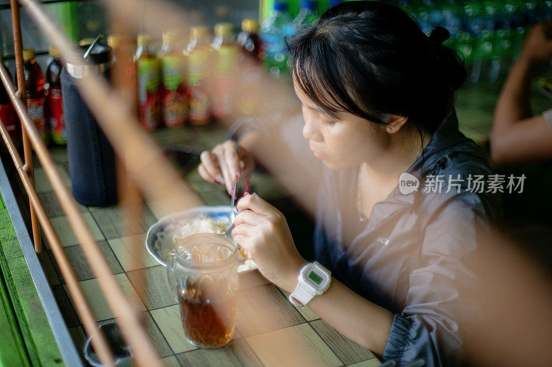 早晨散步后，一个亚洲女孩在钢筋后面的印尼传统小吃摊上吃饭