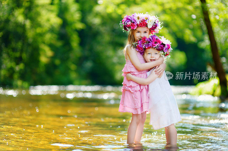两个可爱的小姐妹戴着花冠在夏日的河边