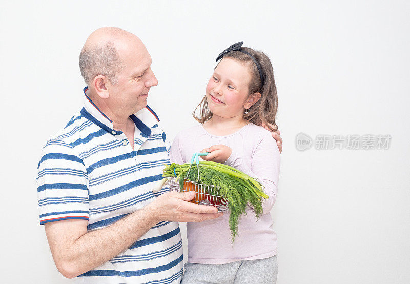 一名男子和一名7岁的白人女孩开心地笑着，手里拿着一篮子新鲜蔬菜。