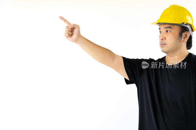 一名戴着黄色安全帽、穿着黑色t恤的亚洲男子正在用手指点一些孤立在白色背景上的东西。