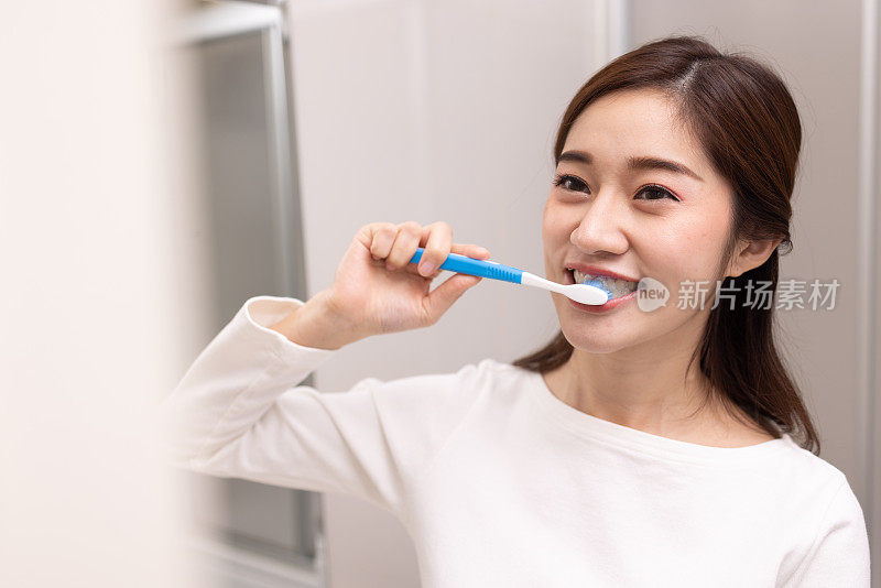 亚洲女人在白色的浴室里清洁牙齿，看起来很开心