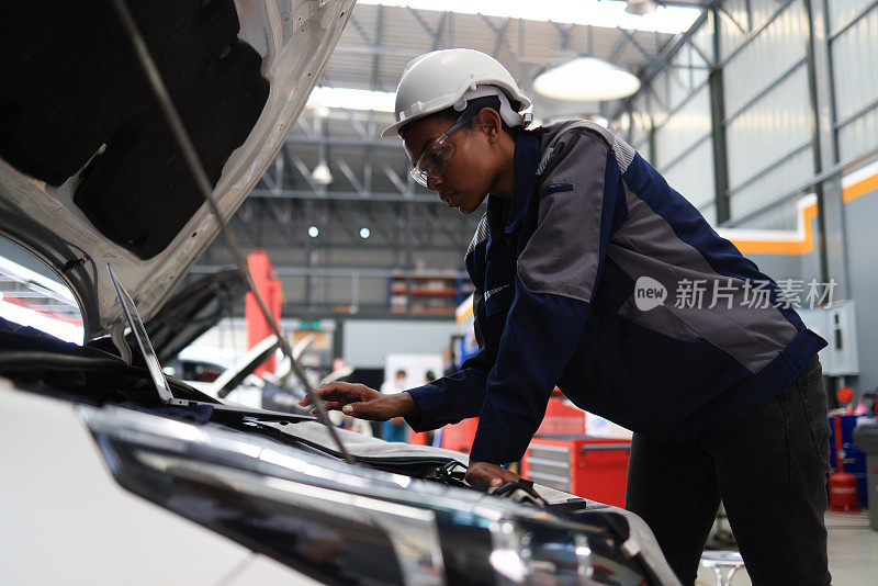 一名亚洲女性在修理厂检查汽车引擎盖下的发动机。