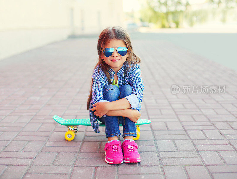 快乐的微笑时尚的小女孩坐在滑板上