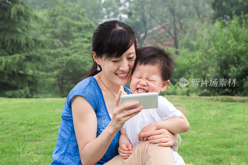 亚洲母亲和婴儿在草地上使用手机