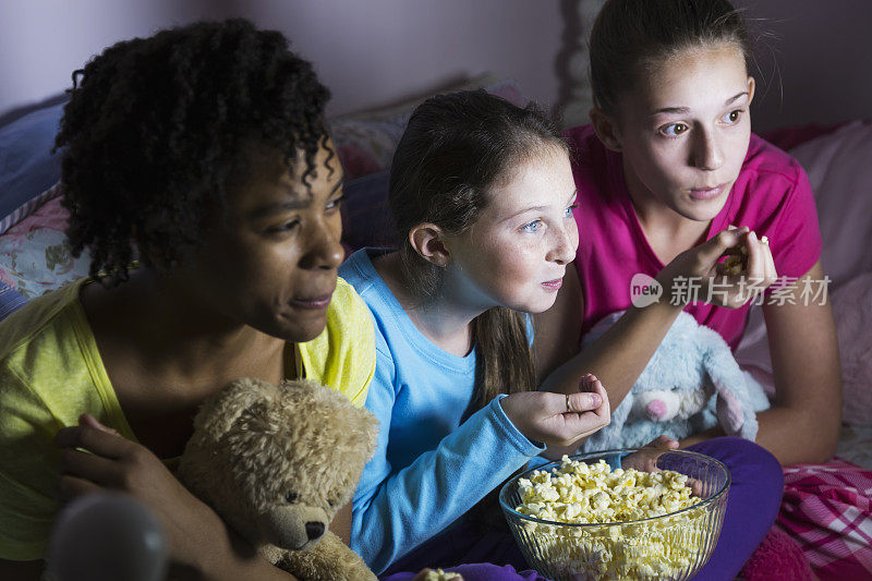 青春期前的女孩在朋友家过夜看电视，吃爆米花