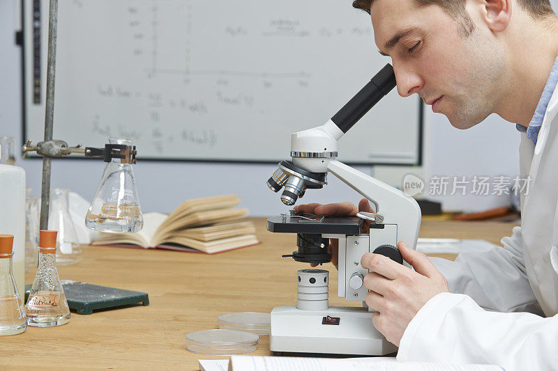男生物老师在教室里透过显微镜看