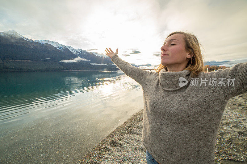 湖边的一位年轻女子伸出双臂，渴望自由