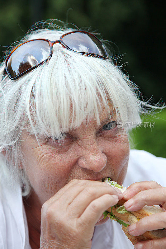 老妇人狼吞虎咽地吃着三明治