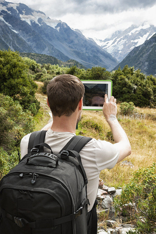 在新西兰南阿尔卑斯山的库克山，徒步旅行者用平板电脑拍照