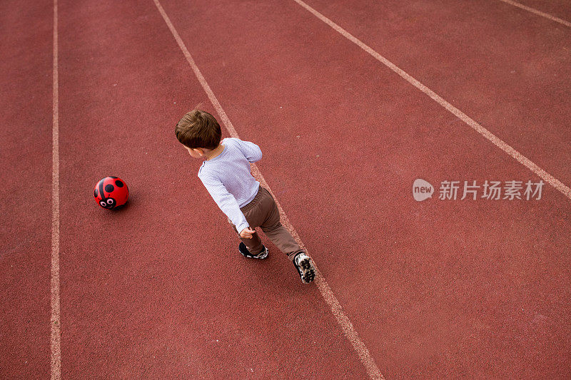 男孩在红色的跑道上踢足球