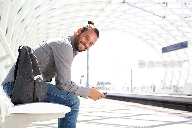 带着手机和背包的微笑男子站在站台上