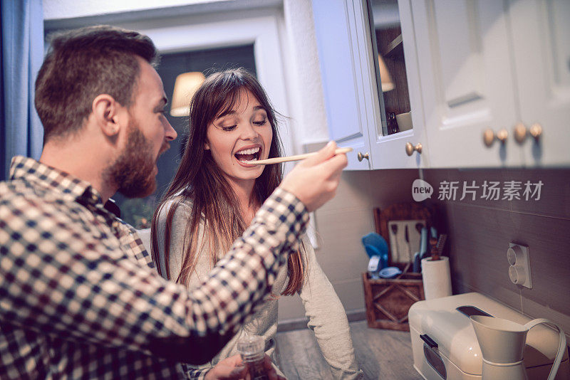 年轻的夫妇在厨房准备晚餐和品尝食物