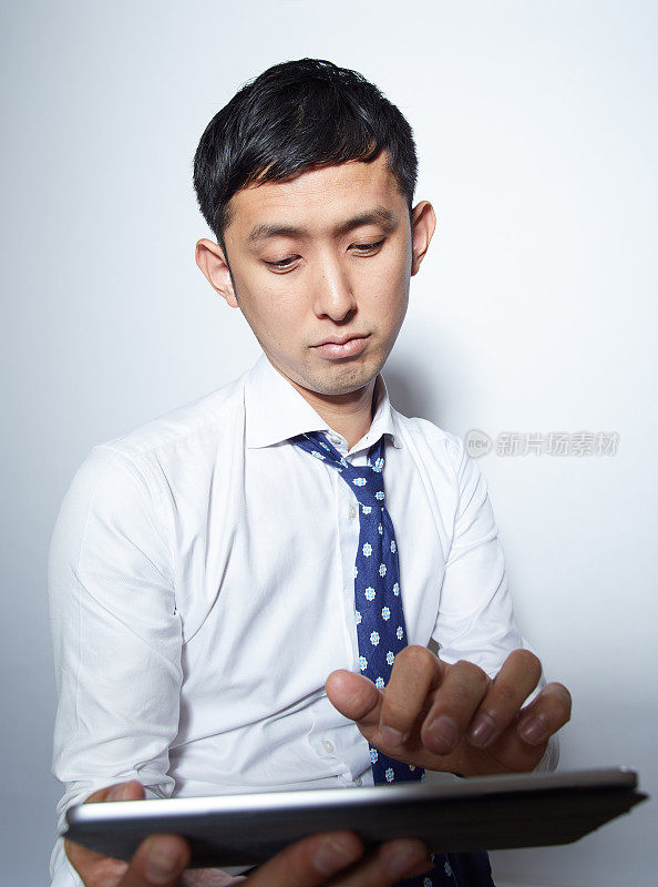穿着西装的年轻日本商人摆弄着他的平板电脑