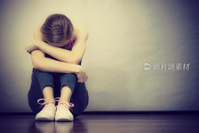 悲伤沮丧的年轻女孩坐在墙边