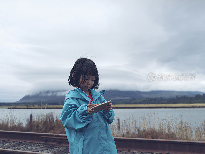 亚洲小孩站在铁路边玩手机